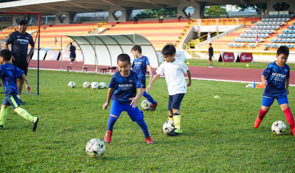 Kids practicing soccer on a field with a coach at a stadium.